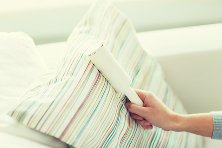 people, housework and housekeeping concept - close up of woman hand with sticky roller cleaning furniture textile or pillowの写真素材