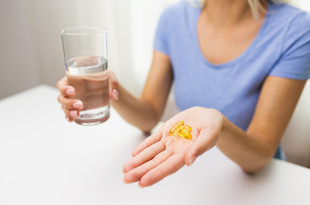 healthy eating, medicine, health care, food supplements and people concept - close up of woman hands holding pills or fish oil capsules and water glass at homeの写真素材