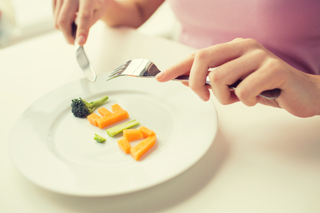 healthy lifestyle, diet, vegetarian food and people concept - close up of woman with fork and knife eating vegetable letters on plateの写真素材