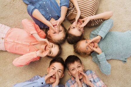 childhood, fashion, friendship and people concept - happy smiling children lying on floor in circle and calling or shoutingの写真素材