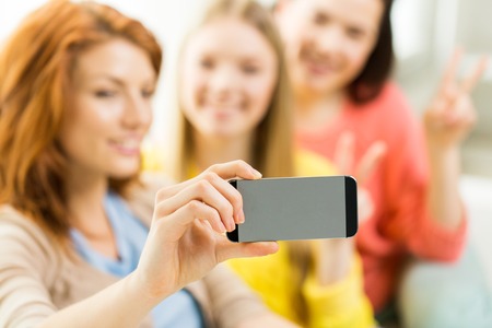 people, technology and leisure concept - close up of young women or teenage friends taking selfie with smartphones at homeの写真素材