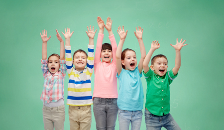 childhood, preschool education, gesture and people concept - happy smiling friends raising fists and celebrating victory over green school chalk board backgroundの写真素材