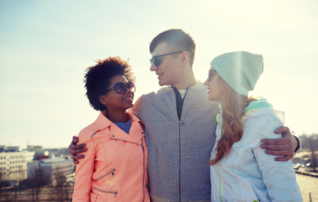 tourism, travel, people, leisure and teenage concept - group of happy friends in sunglasses hugging and talking on city streetの写真素材