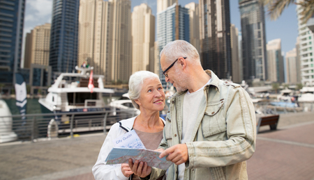 family, age, tourism, travel and people concept - senior couple with map and city guide over dubai harbor or waterfront backgroundの写真素材