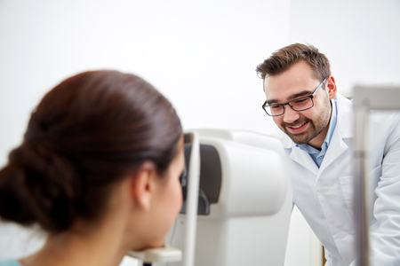 health care, medicine, people, eyesight and technology concept - optometrist with non contact tonometer checking patient intraocular pressure at eye clinic or optics storeの写真素材