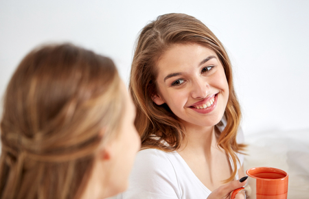 friendship, people, pajama party and communication concept - happy friends or teenage girls drinking, chatting tea and eating sweets at homeの写真素材