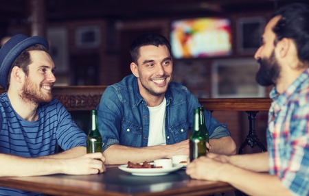 people, leisure, friendship and bachelor party concept - happy male friends drinking bottled beer and talking at bar or pubの写真素材