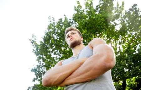 fitness, sport, people and healthy lifestyle concept - sporty young man with crossed arms at summer parkの写真素材