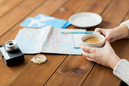vacation, tourism, travel, destination and people concept - close up of hands with coffee cup and travel stuffの写真素材