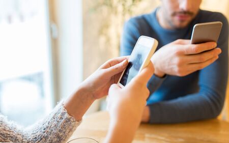 people, communication and technology concept - close up of couple with smartphones drinking tea at...