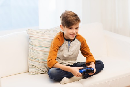 leisure, children, technology and people concept - smiling boy with joystick playing video game at...