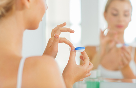 beauty, vision, eyesight, ophthalmology and people concept - close up of young woman applying contact lenses at mirror in home bathroomの写真素材