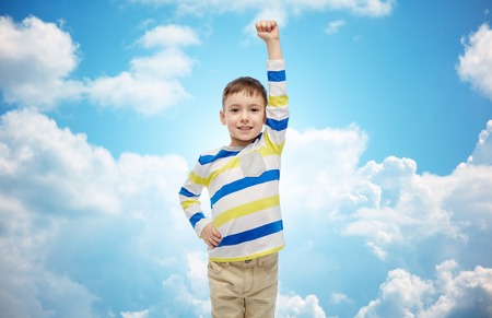 childhood, power, gesture and people concept - happy smiling little boy with raised hand over blue...