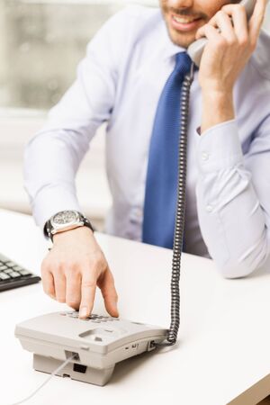 business, people, communication and technology concept - close up of smiling businessman dialing number and calling on phone in officeの写真素材