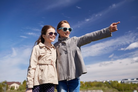people, children, friends and friendship concept -happy little girls in sunglasses hugging and pointing finger outdoorsの写真素材