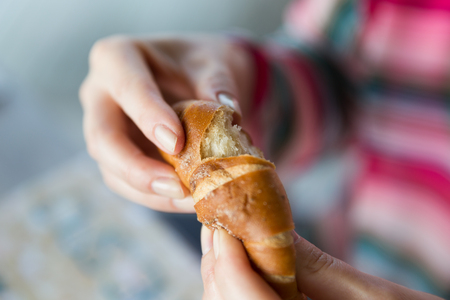 food, baking, people and unhealthy eating concept - close up of woman hands with bun or wheat breadの写真素材