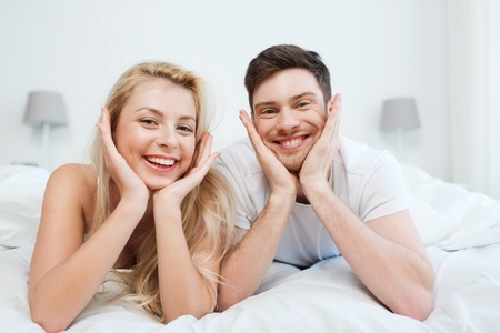 people, rest, love, relationships and happiness concept - happy couple lying in bed at homeの写真素材