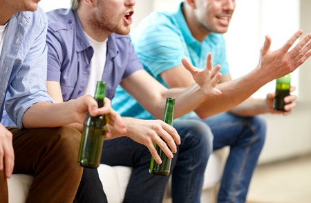 friendship, leisure, people and alcohol concept - close up of happy male friends drinking beer and watching tv at homeの写真素材