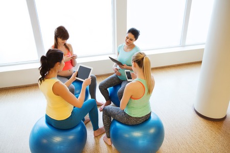 pregnancy, sport, fitness, people and healthy lifestyle concept - group of happy pregnant women with tablet pc computer and smartphone sitting on balls in gymの写真素材