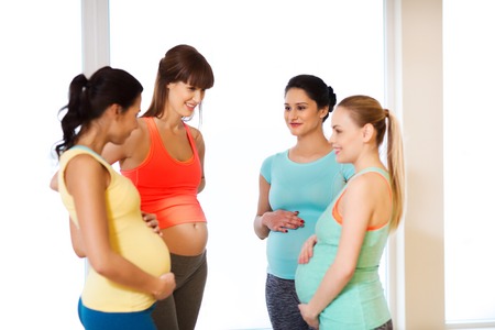 pregnancy, sport, fitness, people and healthy lifestyle concept - group of happy pregnant women talking in gymの写真素材