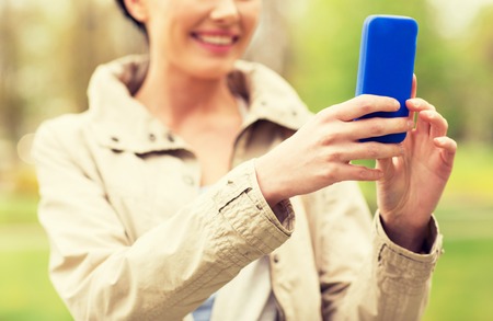 drinks, leisure, technology and people concept - smiling woman taking picture or selfie with smartphone in parkの写真素材