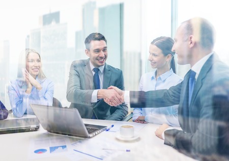 business, technology and office concept - two smiling businessman shaking hands in officeの写真素材