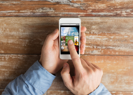 business, internet, mass media, people and technology concept - close up of male hands holding smartphone and pointing finger to web pages screenの写真素材