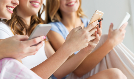 friendship, people, pajama party and technology concept - close up of happy friends or teenage girls with smartphones at homeの写真素材