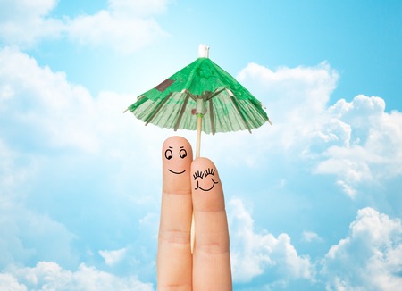 gesture, love, holidays, summer vacation and body parts concept - close up of two fingers with cocktail umbrella decoration over blue sky and clouds backgroundの写真素材