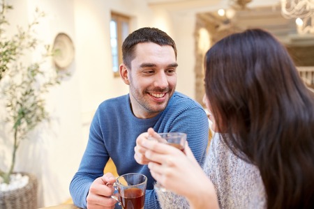people, communication and dating concept - happy couple drinking tea at cafe or restaurant
