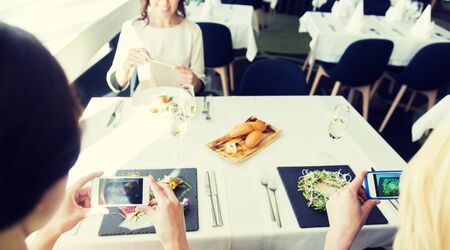 people, holidays, technology and lifestyle concept - close up of women with smartphones taking picture of food at restaurantの写真素材