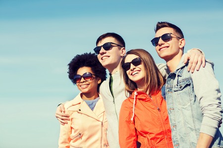 friendship, tourism, travel and people concept - group of happy teenage friends in sunglasses hugging outdoorsの写真素材