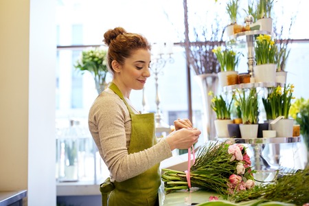 people, business, sale and floristry concept - happy smiling florist woman making bunch at flower shopの写真素材