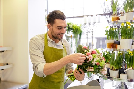 people, business, sale and floristry concept - happy smiling florist man making bunch at flower shop