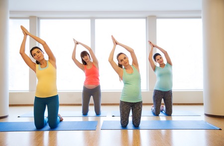 pregnancy, sport, fitness, people and healthy lifestyle concept - group of happy pregnant women exercising on mats in gymの写真素材