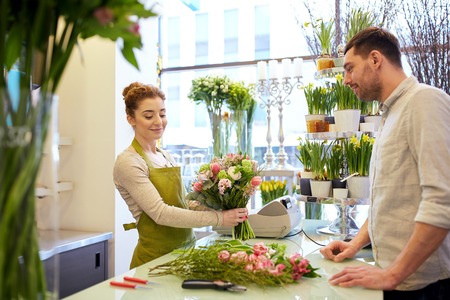people, shopping, sale, floristry and consumerism concept - happy smiling florist woman making bouquet for and man or customer at flower shopの写真素材