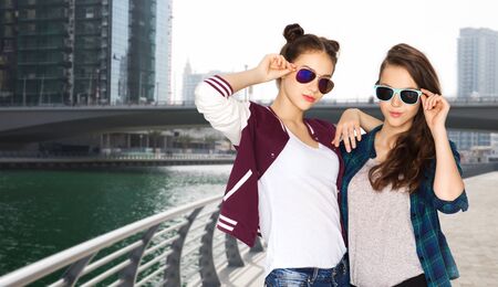 people, travel, tourism, fashion and teens concept - happy smiling pretty teenage girls oe friends in sunglasses over dubai city street backgroundの写真素材