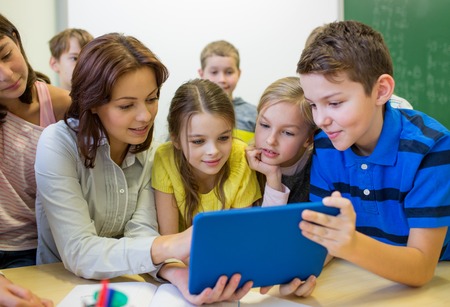 group of school kids with teacher looking to tablet pc computer in classroomの写真素材