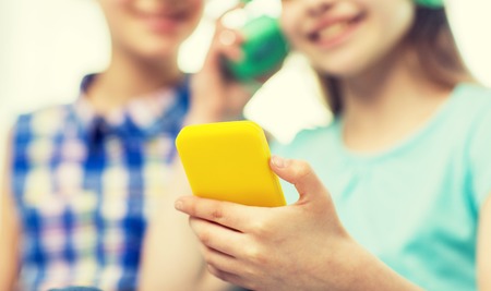 close up of happy little girls with smartphone and earphones listening to music