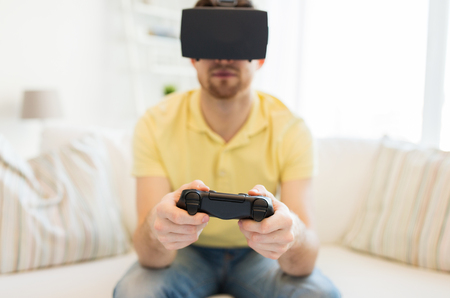 3d technology, virtual reality, gaming, entertainment and people concept - close up of happy young man with virtual reality headset or 3d glasses playing video game with controller gamepad at homeの写真素材
