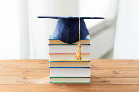 education, school, graduation and knowledge concept - close up of books and mortarboard on wooden tableの写真素材