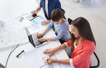 business, startup and people concept - happy creative team with laptop and blueprint at office