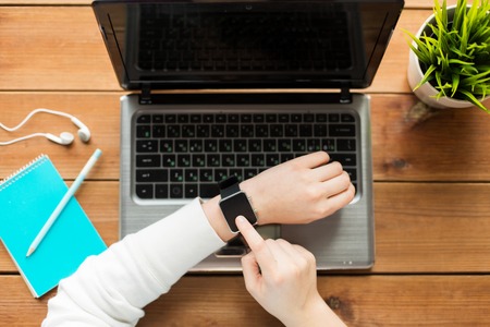 education, business, people and technology concept - close up of woman with smart watch and laptop computer on wooden tableの写真素材