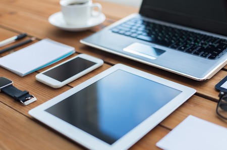 education, business and technology concept - close up of on laptop computer, tablet pc, notebook and smartphone on wooden tableの写真素材