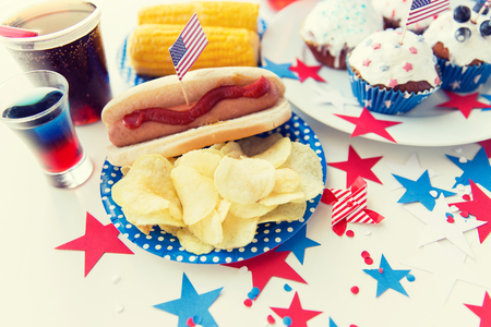 national holidays, celebration, food and patriotism concept - close up of hot dog with american flag decoration, potato chips and drinks on 4th july at party on independence dayの写真素材