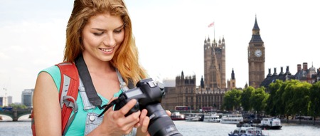 travel, tourism and people concept - happy young woman with backpack and camera photographing over...