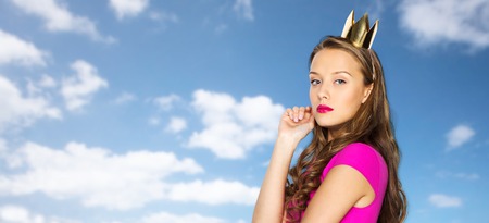 people, holidays and fashion concept - young woman or teen girl in pink dress and princess crown...