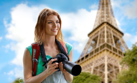 travel, tourism and people concept - happy young woman with backpack and camera photographing over eiffel tower backgroundの写真素材