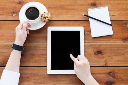 business, education, technology and people concept - close up of woman with blank tablet pc computer screen, notebook and coffee on wooden tableの写真素材