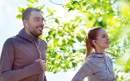 fitness, sport, people, technology and lifestyle concept - happy couple running and listening to music in earphones over green natural backgroundの写真素材
